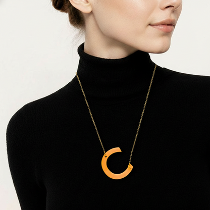 Person wearing a black turtleneck with a gold necklace featuring an orange pendant against a white background